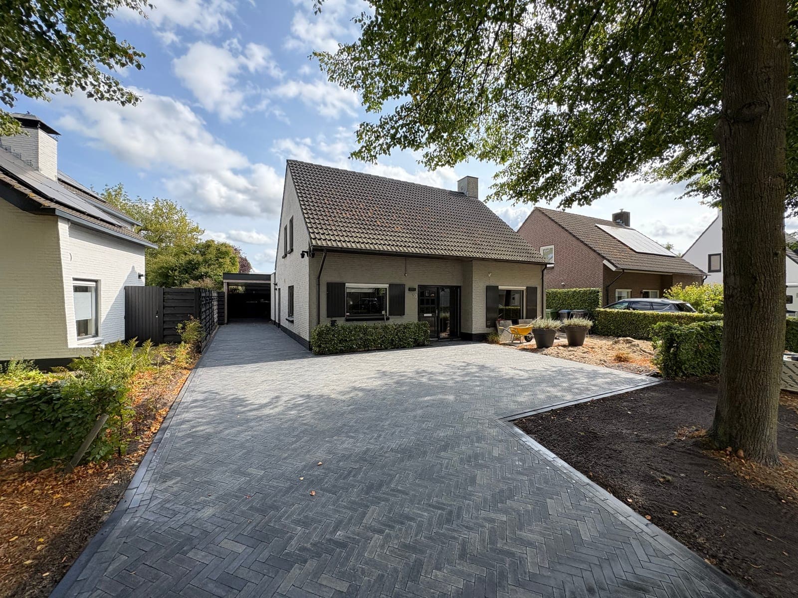 Afgeronde oprit in grijze klinkers bij een woning met hagen en bomen