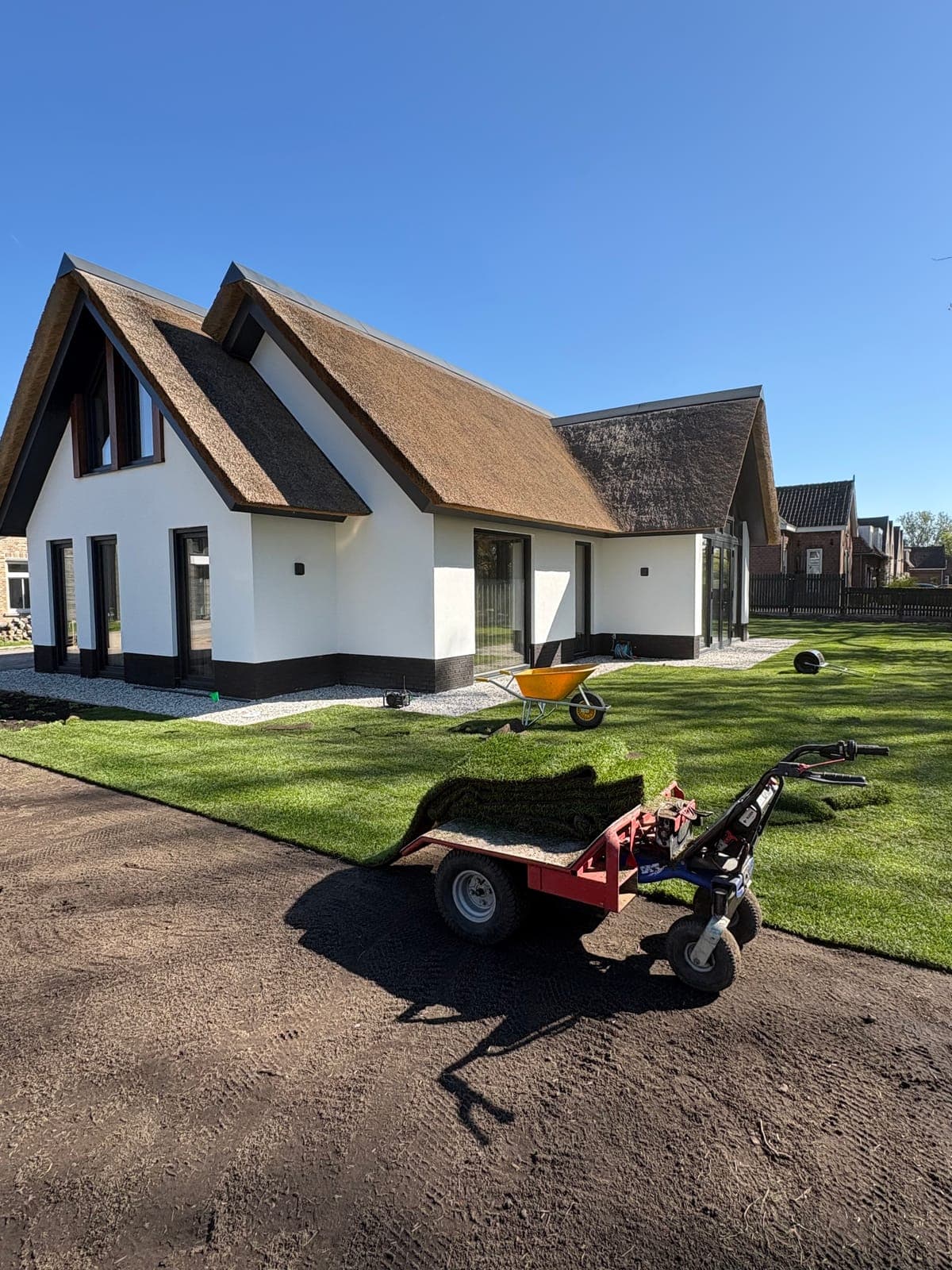 Nieuwe graszoden worden gelegd rondom een rietgedekte woning