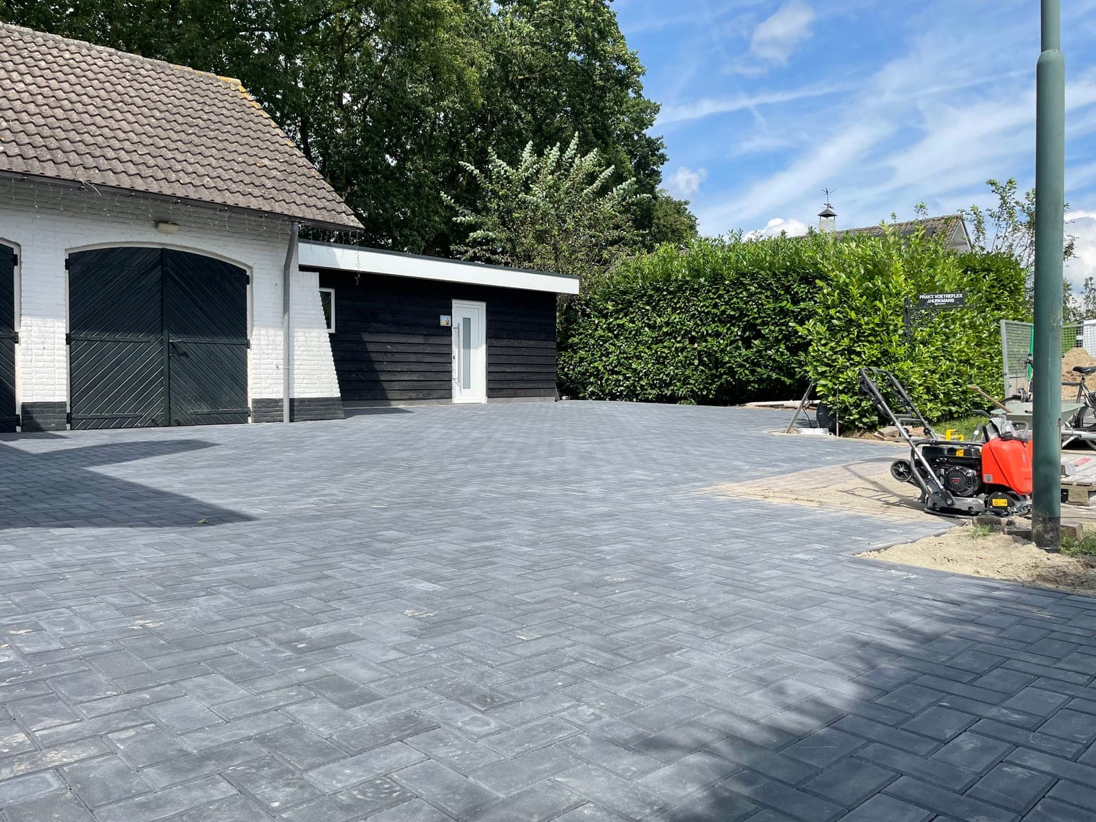 Afgeronde oprit in grijze betonklinkers met haag en garage