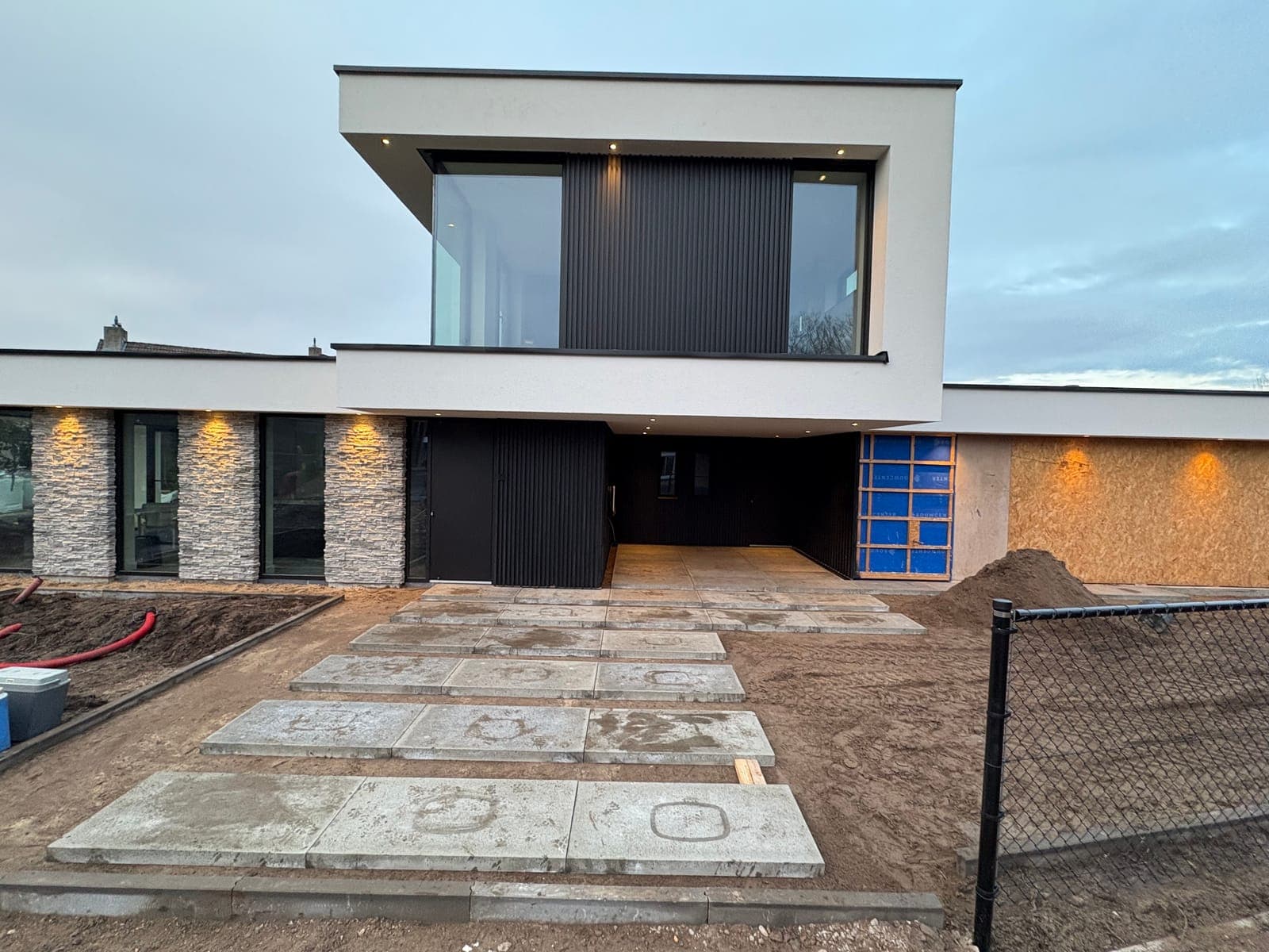 De villa in de avond, met verlichte carport en bestrating in grote platen