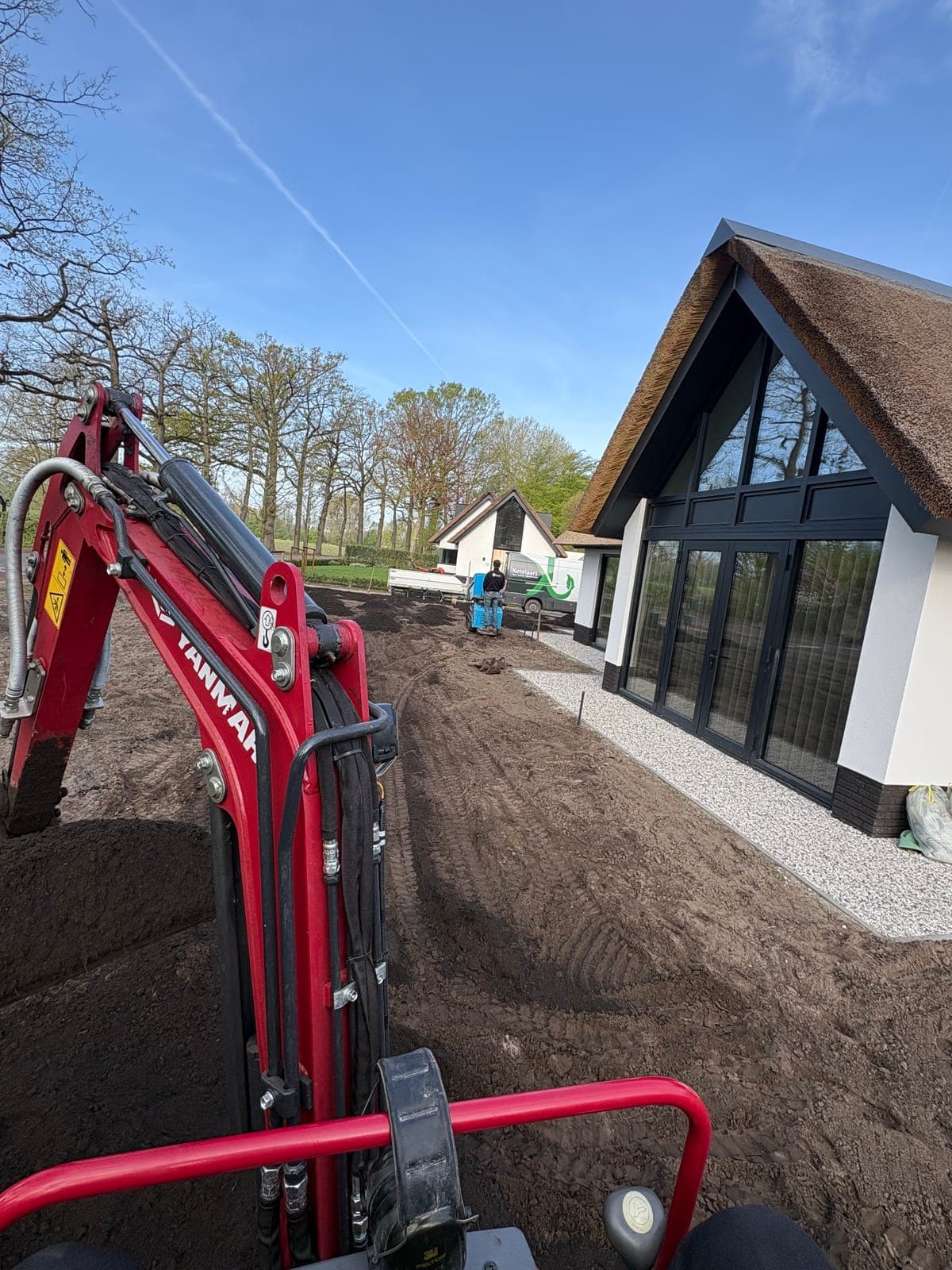 Grondwerk met graafmachine bij de rietgedekte woning